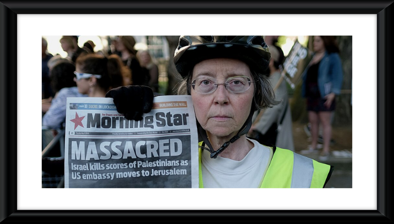  A London activist selling the Morning Star holds up the paper's headline on the violence by the Israeli army on the day of the relocation of US Embassy in Israel from Tel Aviv to Jerusalem; 61 unarmed Palestinians, including several children and a baby, were killed by the Israeli army, most of them shot dead by precision snipers during a demonstration close to Gaza's border fence. Over 2,000 were injured.-SOURCE:  WIKIPEDIA