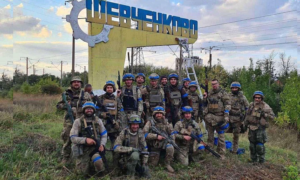 Territorial Defence Forces of Ukraine soldiers near the freshly repainted (from Russian flag colors back to Ukrainian ones) entrance mark in Shevchenkove liberated from Russian army-wikipedia